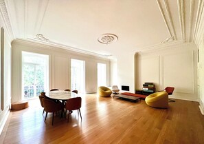 A spacious living room with a wooden floor, a round dining table with chairs, and a sofa. - Luxury 3-Bedroom Apartment in Prime Central Lisbon | Terrace, Pool, Gym, and Private Parking (Lisboa)