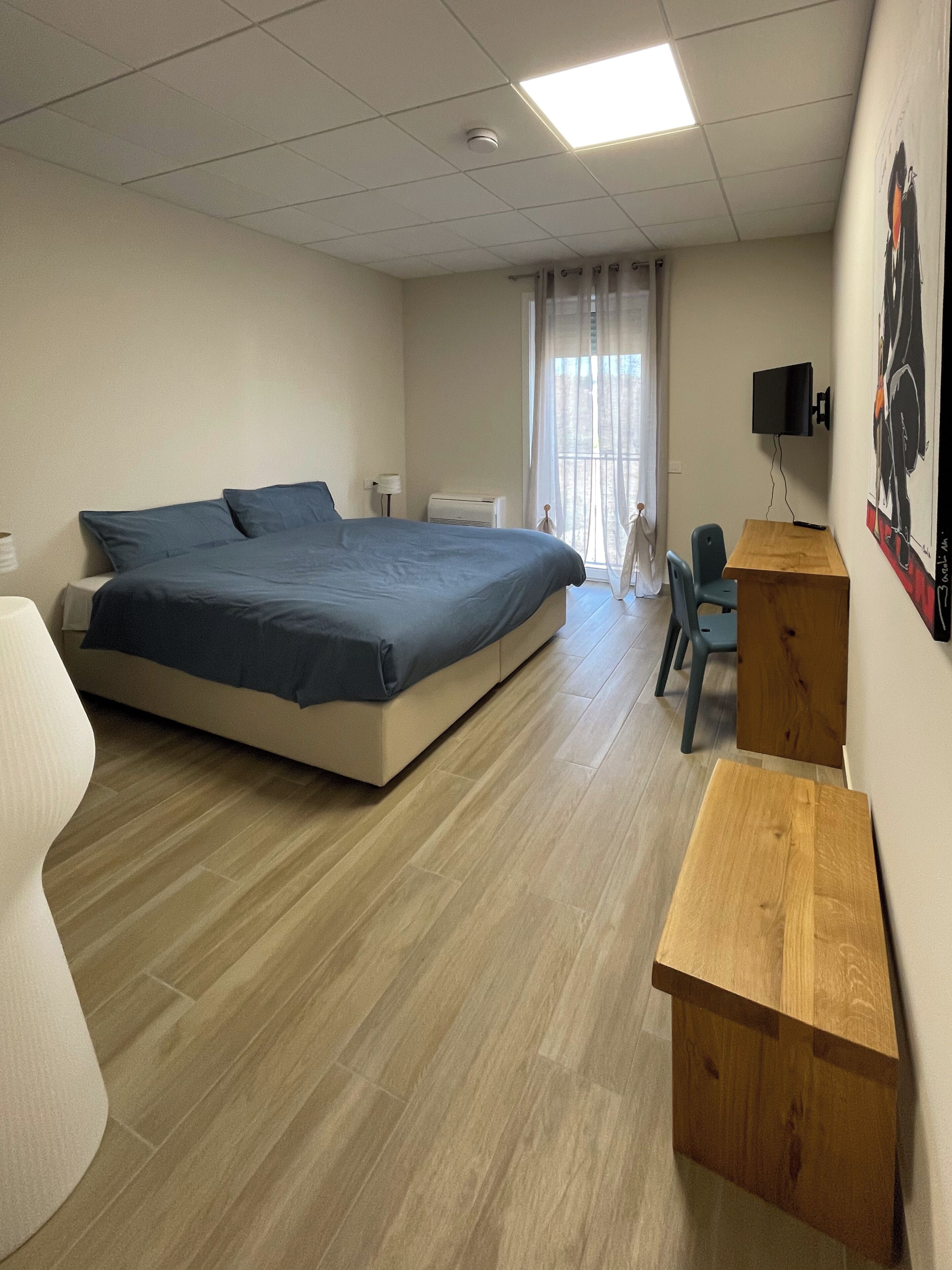 A bedroom with a bed, a desk, a chair, a TV, and a window with curtains.