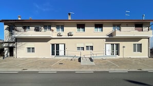 Um edifício de dois andares com varandas, aparelhos de ar condicionado e portão fechado.