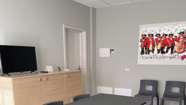 Uma sala de conferências com uma mesa comprida, seis cadeiras, um armário de madeira, uma televisão e um cartaz na parede.