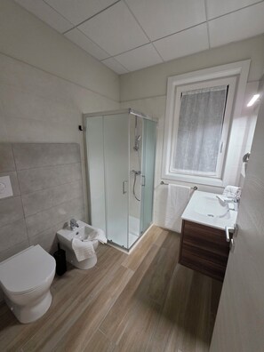 Ett modernt badrum med en dusch som är avskärmad med glasväggar, ett vitt handfat och en toalett.
