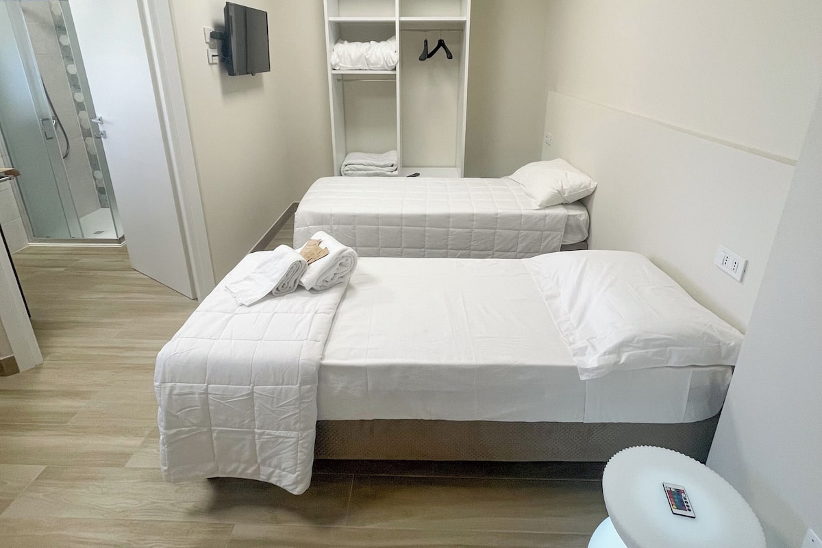 Une chambre d’hôtel avec deux lits, une armoire, une table de chevet et un luminaire moderne.