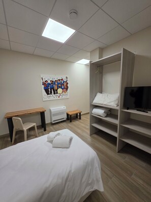A hotel room with a bed, a desk, a chair, a TV, and a shelf with towels. - Mama Lidia (ITALY)