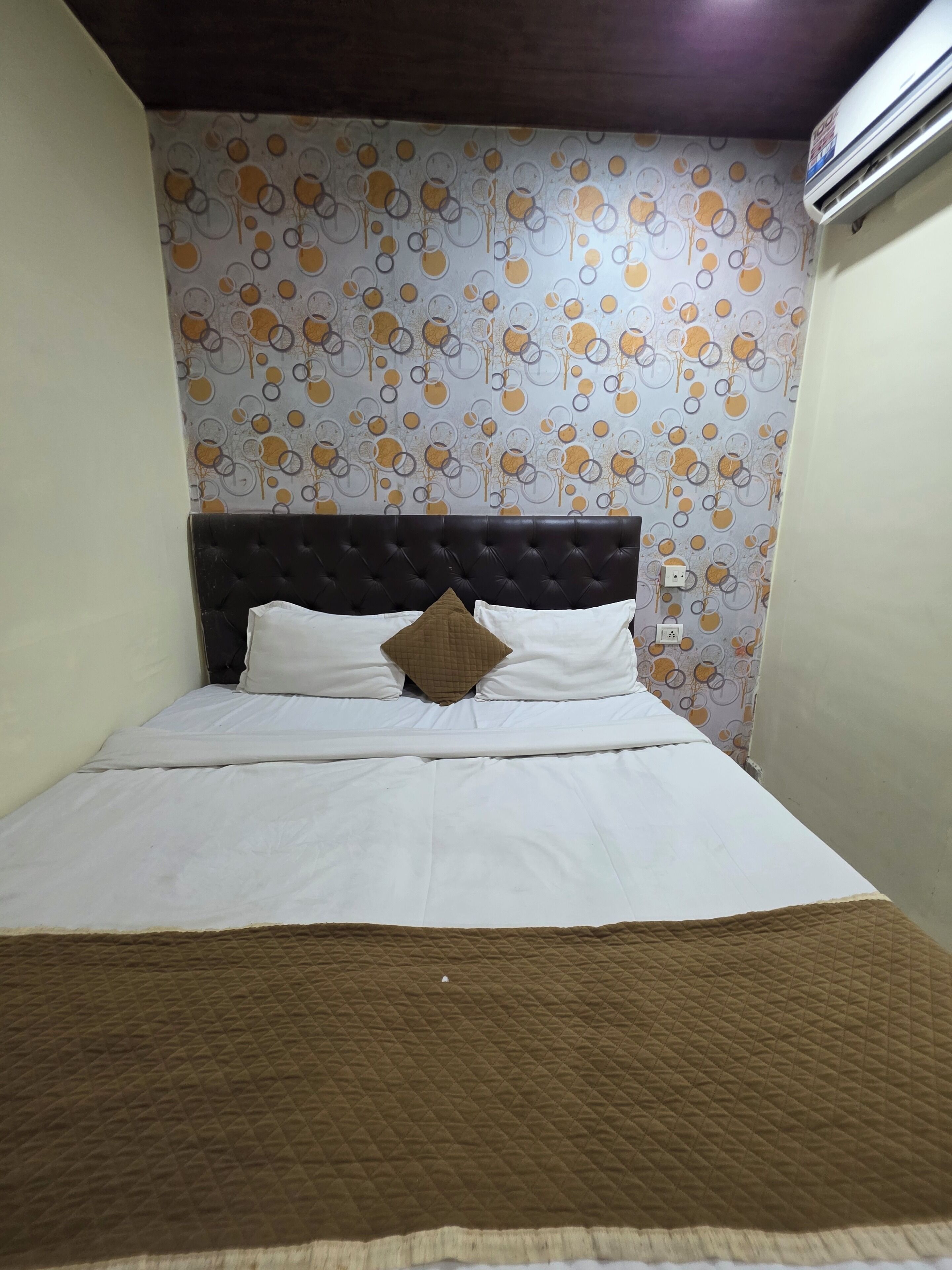 A bed with a dark headboard, white bedding, and a brown quilted bedspread.