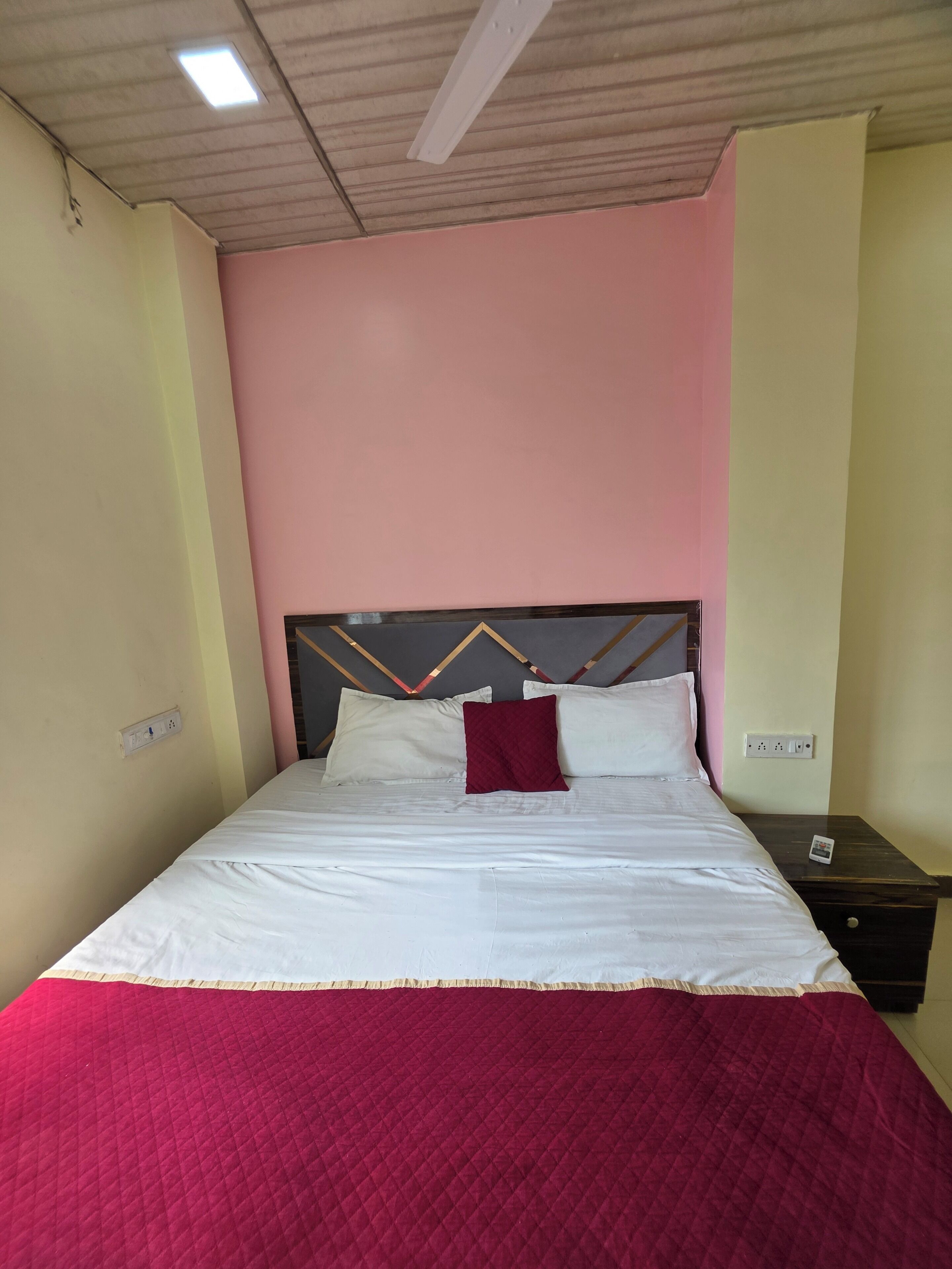 A hotel room with a bed, a nightstand, and a wall socket.