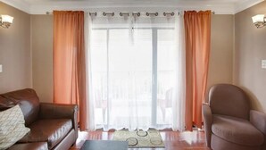 En stue med en brun lædersofa, en brun lænestol og et stort vindue med orange gardiner.