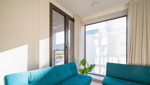 A modern living room with two teal sofas, a large window with curtains, and a potted plant. - Elegant City Hub for 8 With Terrace (Antwerp)