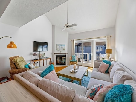 A living room with a sofa, a coffee table, a television, a fireplace, and a balcony with a view.