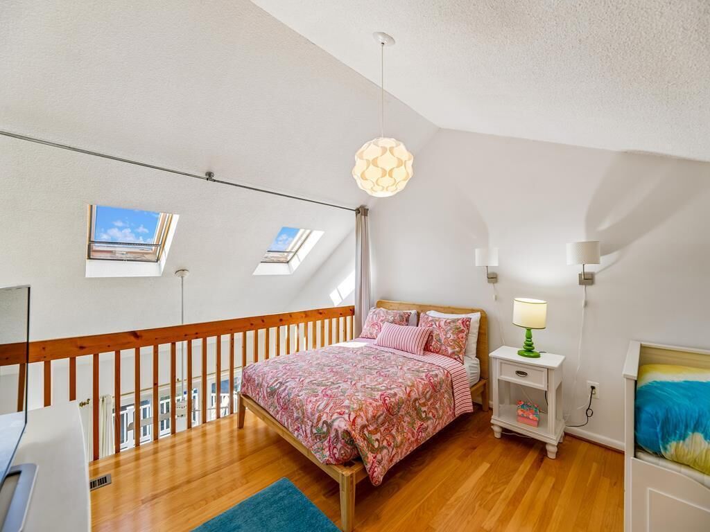 Een slaapkamer met een houten bed, een nachtkastje, een lamp en een uitzicht op de lucht door dakramen.