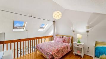 Een slaapkamer met een houten bed, een nachtkastje, een lamp en een uitzicht op de lucht door dakramen.