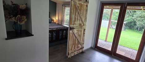 A room with a bed, a sliding door leading to a balcony, and a small shelf with a vase.