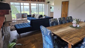 A spacious living area with a wooden dining table, blue upholstered furniture, and a large sliding glass door leading to a balcony.