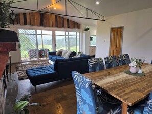 A spacious living area with a wooden dining table, blue upholstered furniture, and a large sliding glass door leading to a balcony.