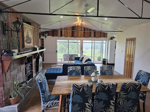 A spacious living area with a fireplace, a dining table with chairs, a sofa, and a view through large sliding glass doors to the outdoors.