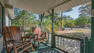 A covered porch with wooden rocking chairs, a lattice railing, and a view of a park with trees and a street.