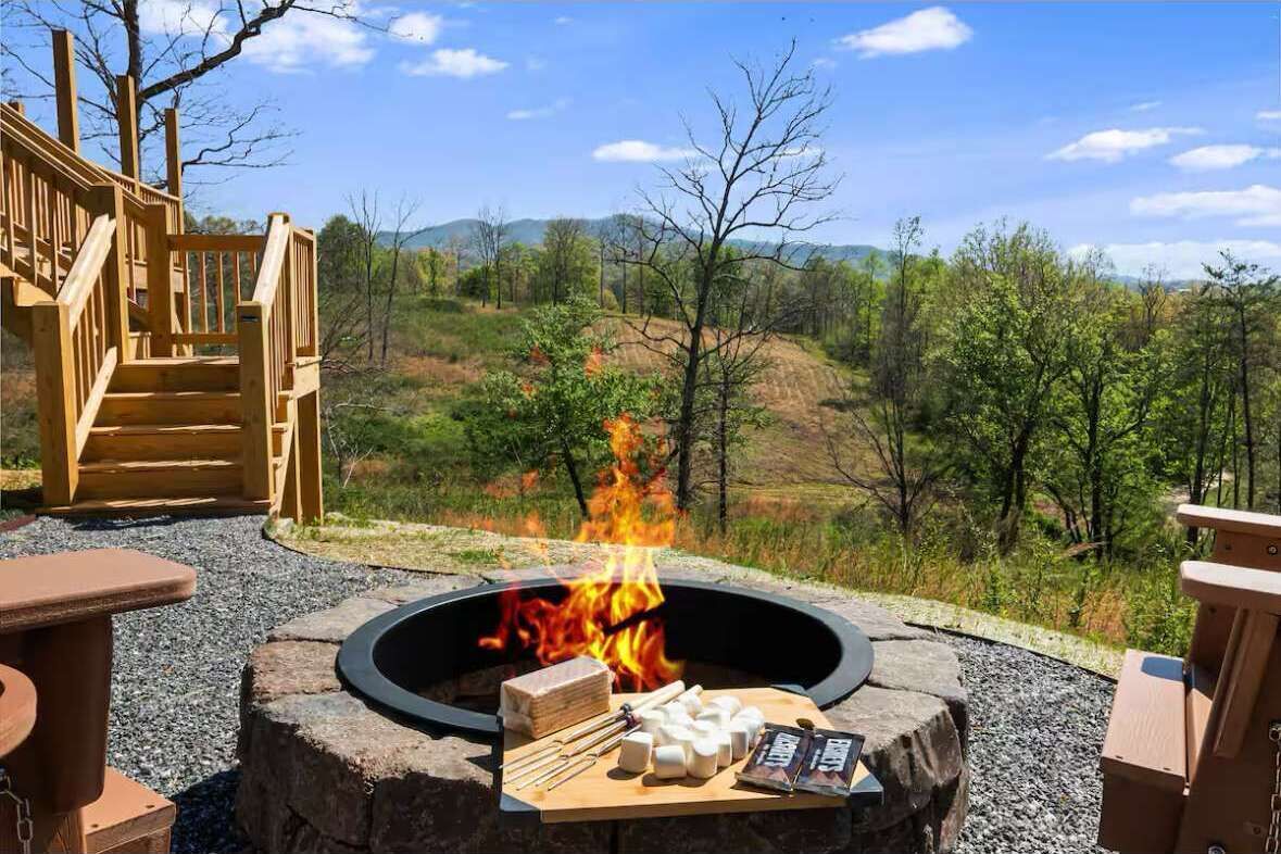 A fire pit with a wooden deck, outdoor seating, and a view of a hilly landscape.