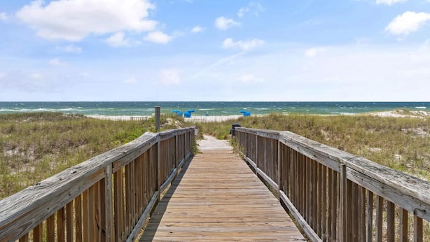 A wooden boardwalk leading to the beach with a clear view of the ocean and dunes. - Needle Rush Point E13 (Pensacola)