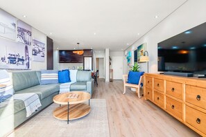 Ein modernes Wohnzimmer mit Sofa, Couchtisch, Fernseher, Holzschrank und Kunstwerken an den Wänden.