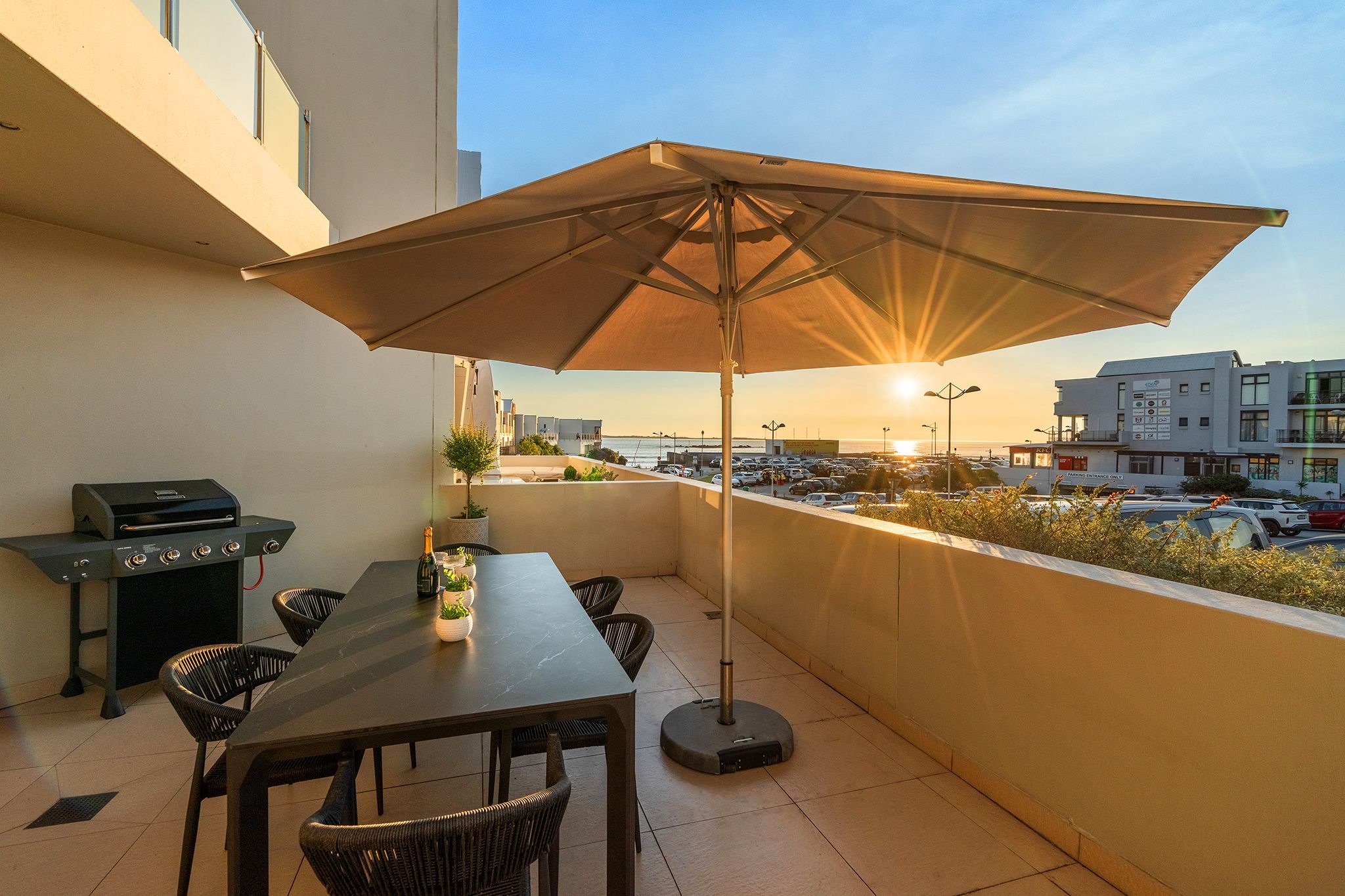 An outdoor patio with a table, chairs, a grill, and an umbrella.