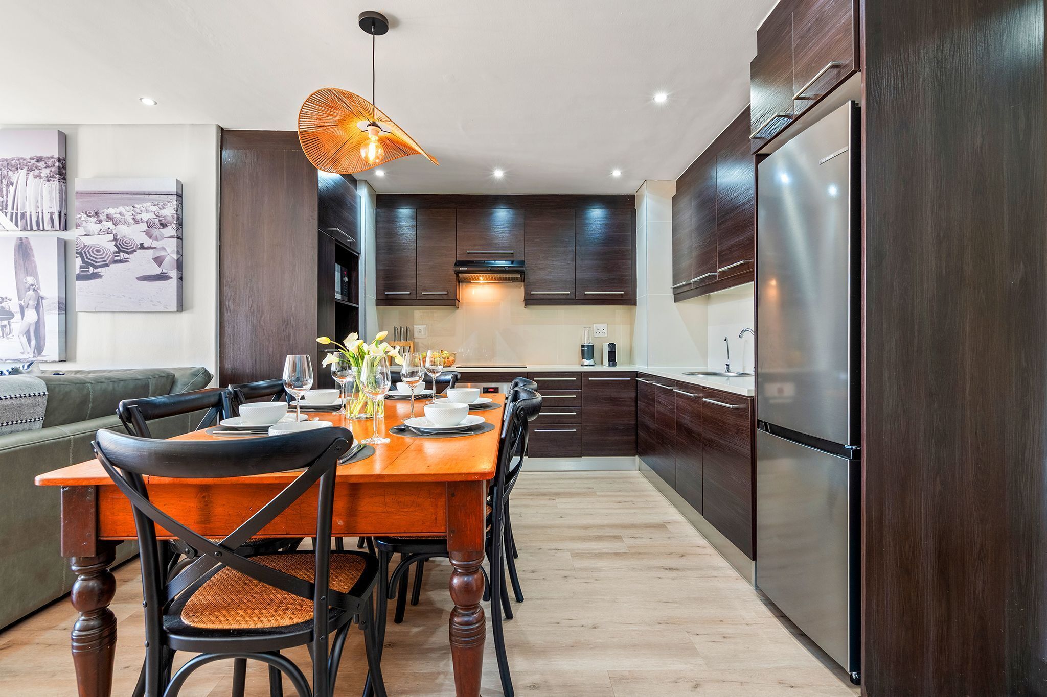 Une cuisine moderne avec des meubles de couleur bois foncé, un réfrigérateur en acier inoxydable et un coin repas comprenant une table et des chaises en bois.