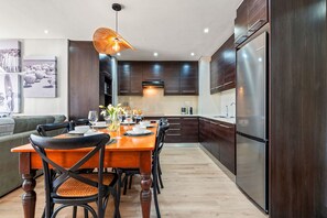 A modern kitchen with dark wood cabinets, a stainless steel refrigerator, and a dining area with a wooden table and chairs. - Ocean Mist 105 (Cape Town)