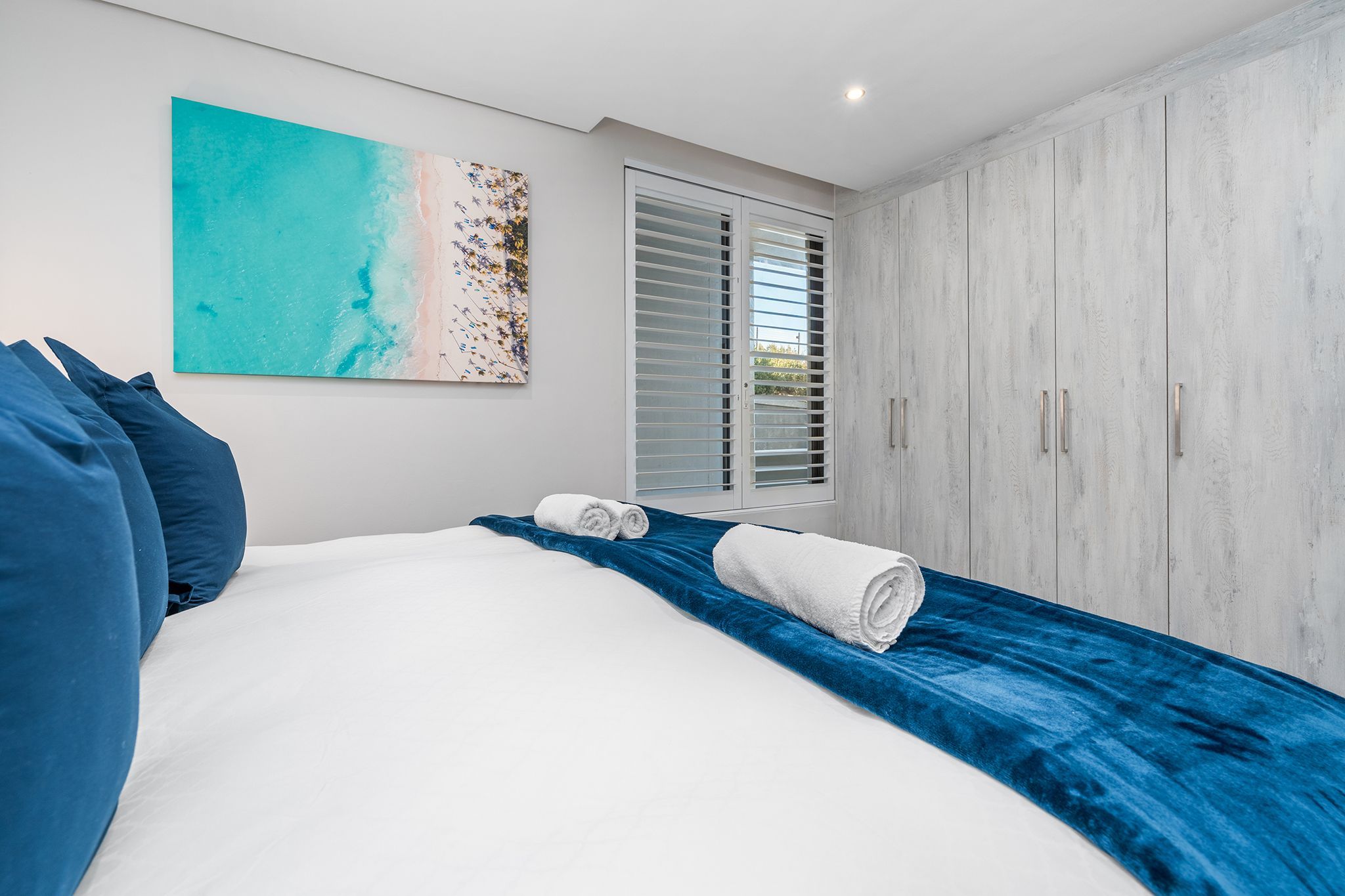 Ein Schlafzimmer mit einem Bett, einem großen Gemälde, einem Kleiderschrank und einem Fenster mit Jalousien.