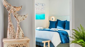 Ein Schlafzimmer mit Bett, Kissen, Nachttisch, Wandbild und Pflanze.
