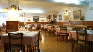 A restaurant with multiple tables and chairs, wooden paneling, and wall-mounted light fixtures. - Hostal Pirineos Meliz (Bielsa)