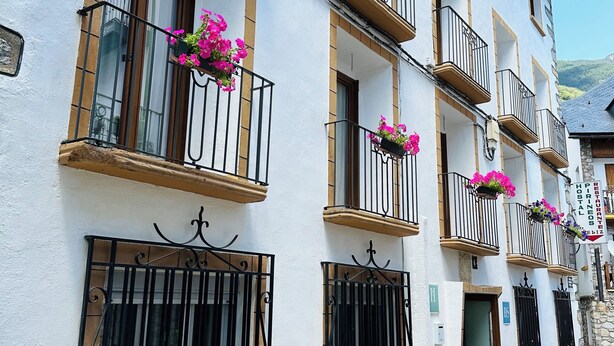 A multi-story building with balconies, potted plants, and a sign indicating a restaurant. - Hostal Pirineos Meliz (Bielsa)