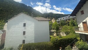 A white building with multiple windows, surrounded by greenery and a mountainous backdrop. - Hostal Pirineos Meliz (Bielsa)