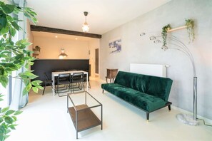 A modern living room with a dark green sofa, a glass coffee table, a dining table with chairs, a pendant light, and a floor lamp. - Antwerp Central 1br/7p Apartment (Antwerp)