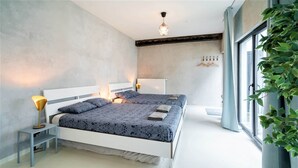 A bedroom with a bed, bedside tables, a radiator, and a window with a plant. - Antwerp Central 1br/7p Apartment (Antwerp)