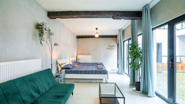 A modern bedroom with a bed, a green sofa, a glass coffee table, and large windows. - Antwerp Central 1br/7p Apartment (Antwerp)
