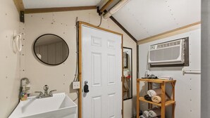 A bathroom with a white sink, a mirror, a wooden shelf with towels, and a white door.