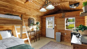 A wooden cabin with a bunk bed, a desk, a chair, a window with a view, and a door.