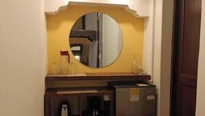 Una kitchenette compacta con refrigerador, cafetera y espejo sobre la encimera.