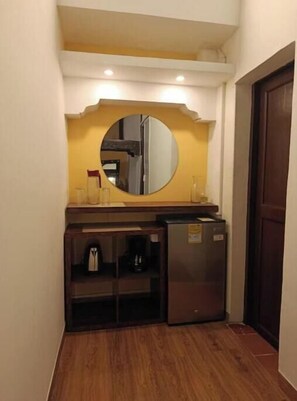 Eine kompakte Küchenzeile mit einem Kühlschrank, einer Kaffeemaschine und einem Spiegel über der Arbeitsfläche.
