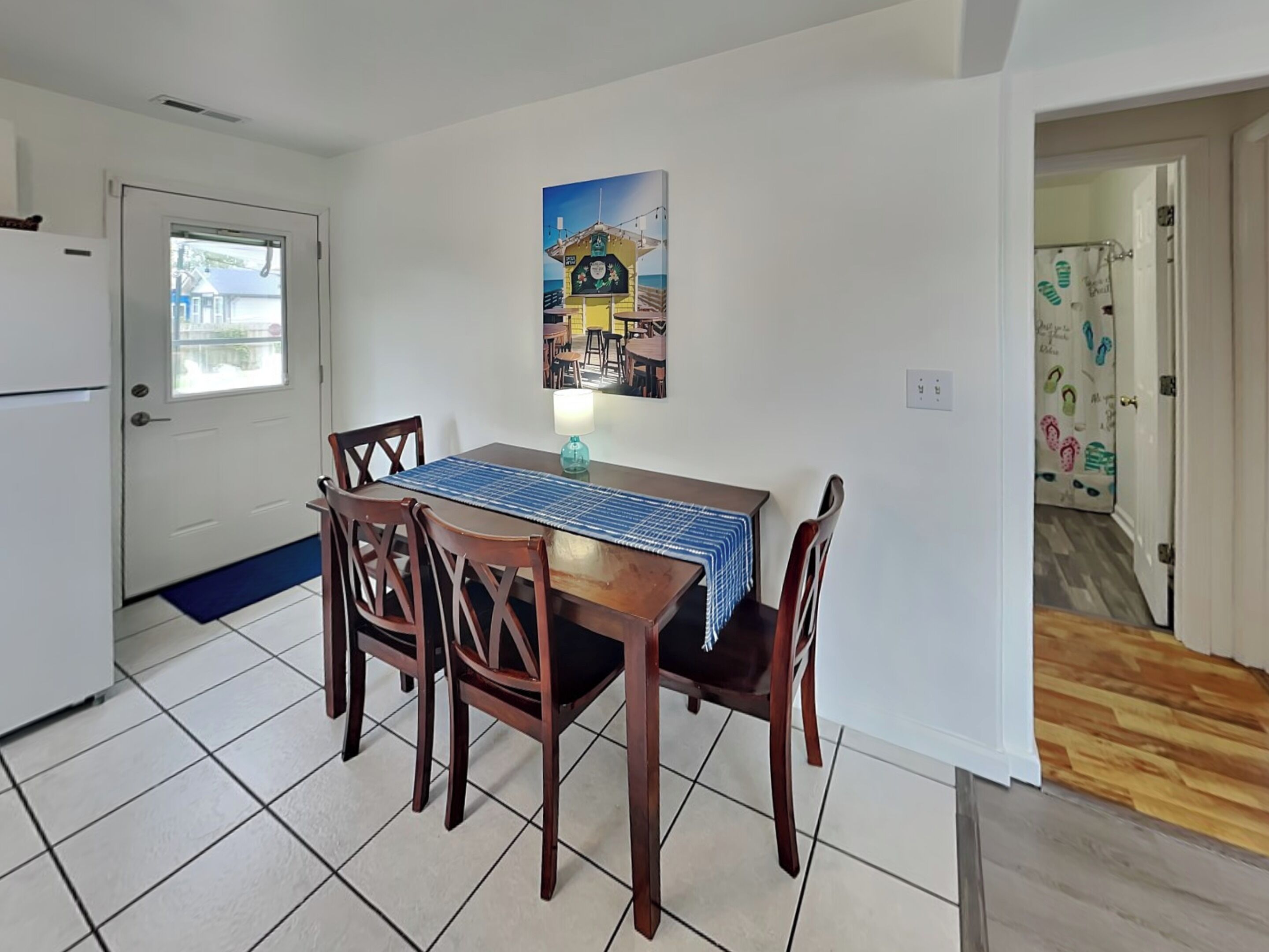 A dining area with a table, chairs, a blue tablecloth, and a wall-mounted painting.