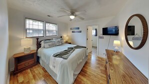 A bedroom with a bed, bedside tables, a ceiling fan, a TV, a mirror, and a door.