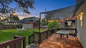 A patio with a table and chairs, a wooden fence, and a covered area with string lights.