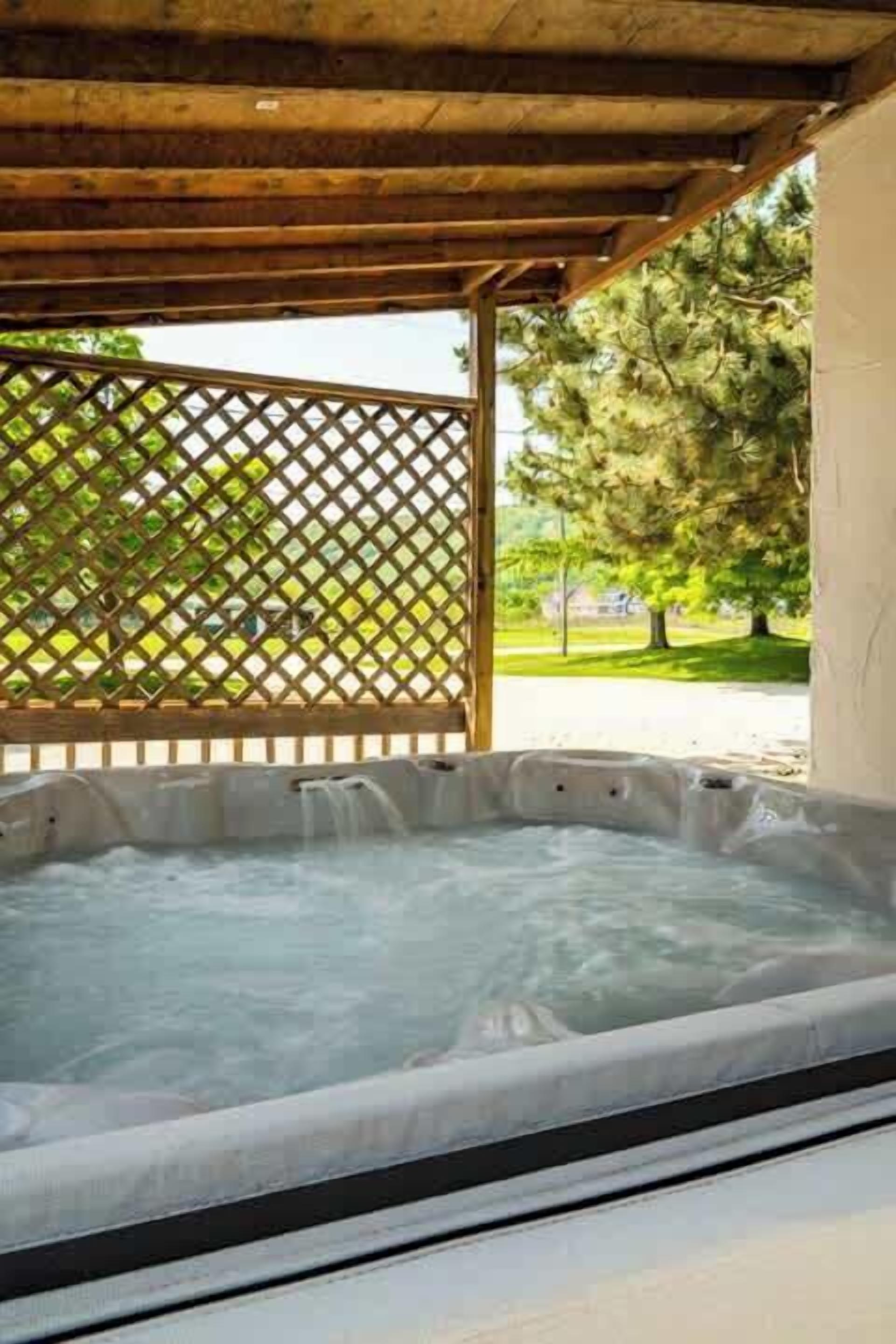 A hot tub under a wooden pergola with a lattice fence in the background.