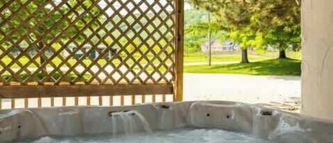 A hot tub under a wooden pergola with a lattice fence in the background.