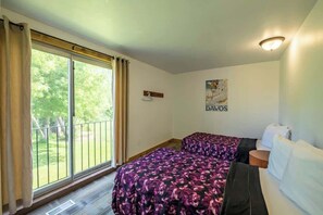 Ein Schlafzimmer mit zwei Betten, einem fensterbelaubten Fenster, einer Wandleuchte und einem Poster.