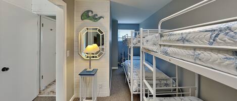 A room with bunk beds, a mirror, a lamp, and a door leading to another room.