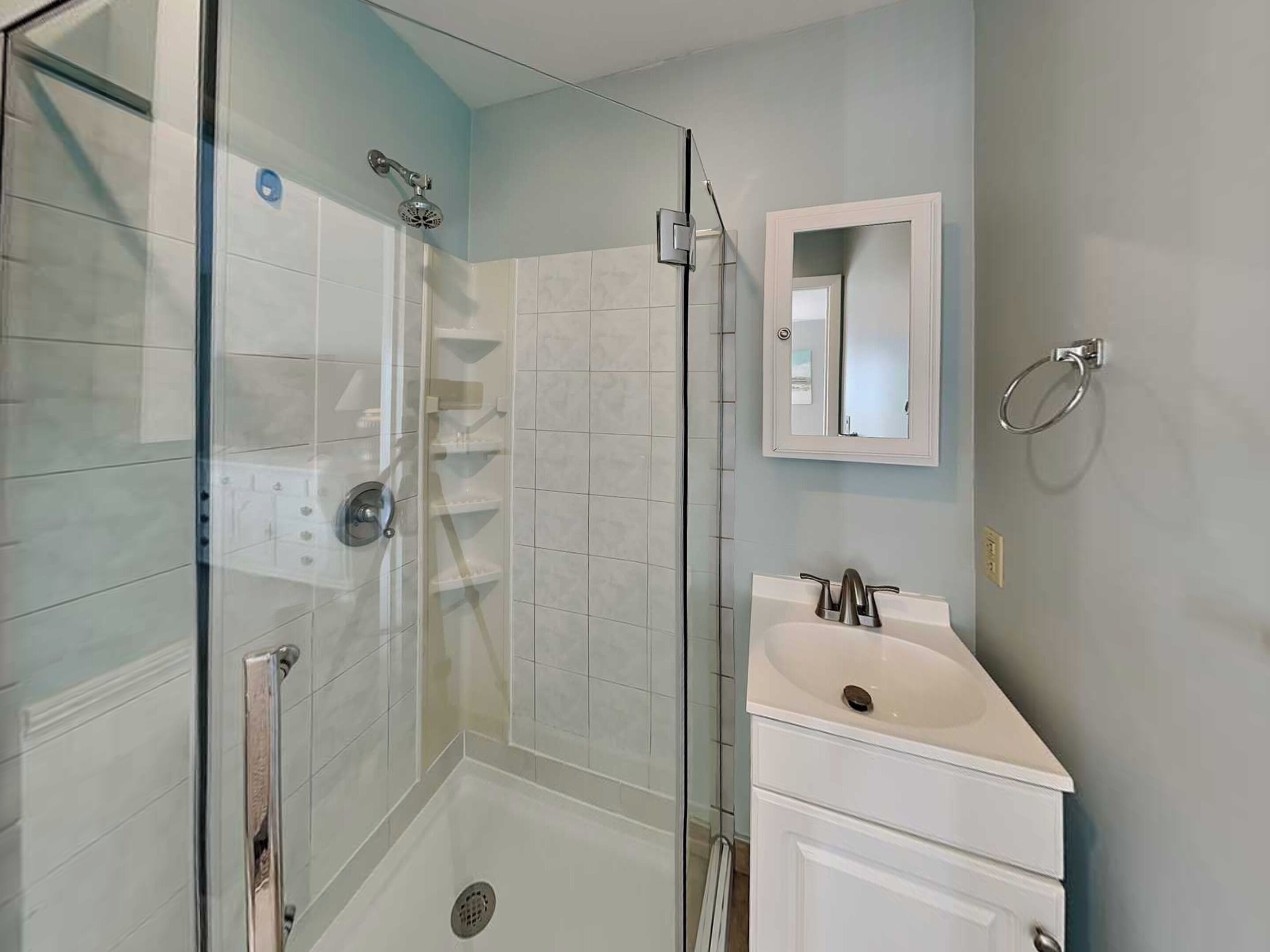 Un baño moderno con ducha envuelta en vidrio, un lavamanos blanco y un espejo sobre él.