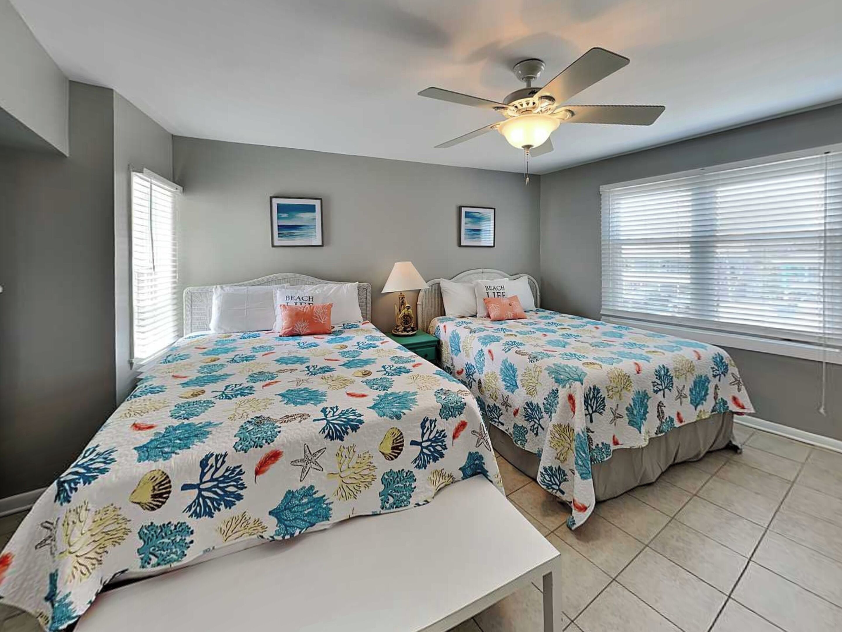 A bedroom with two beds, a ceiling fan, and a window with blinds.