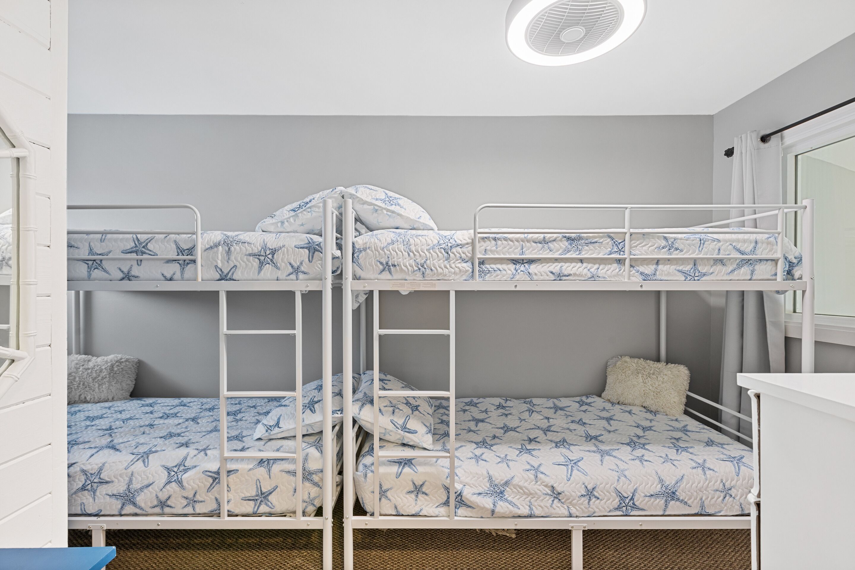 A bunk bed room with star-patterned bedding, a ceiling fan, and a window with curtains.