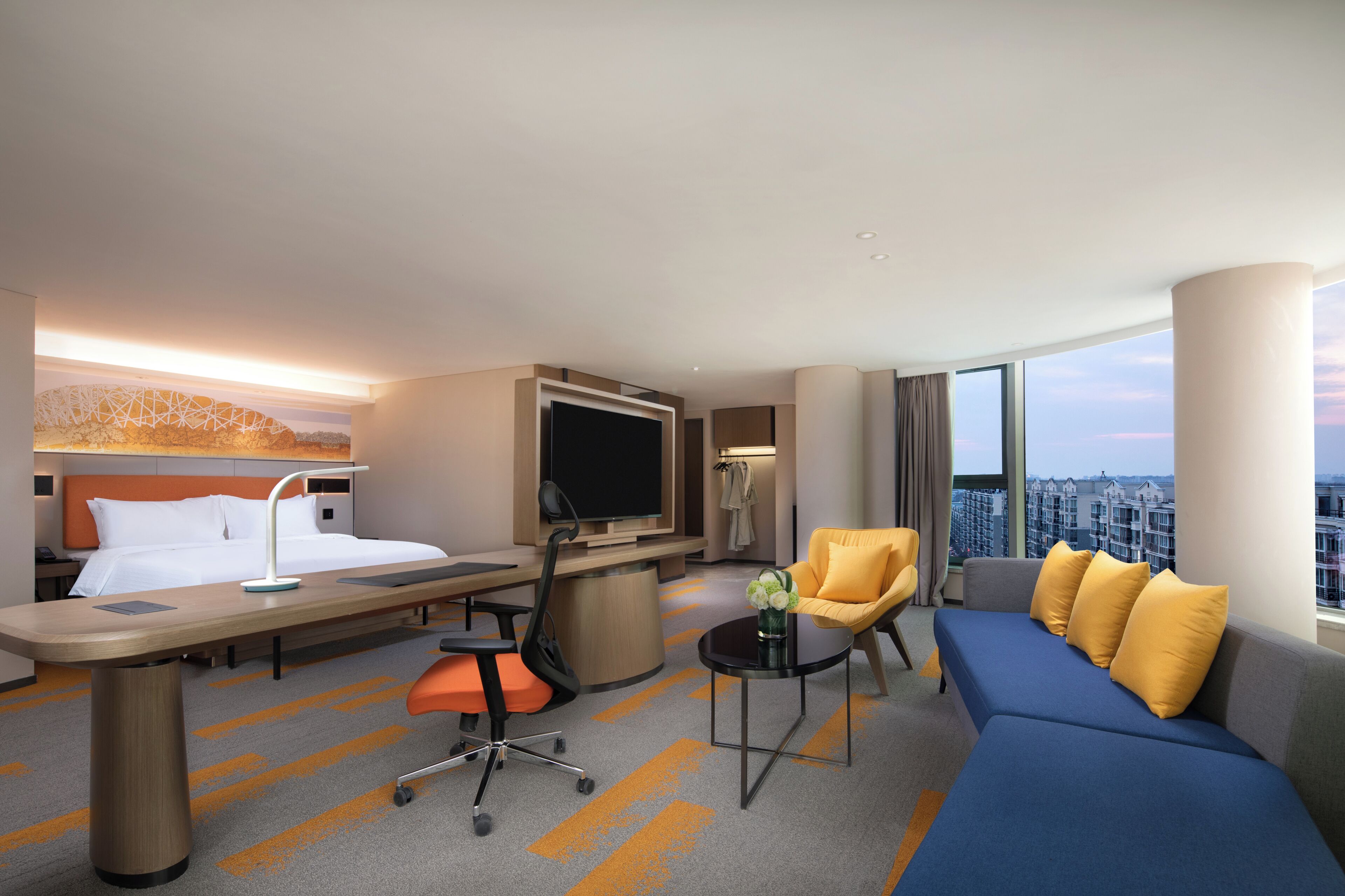 Habitación de hotel con cama, escritorio, silla, sofá, televisión y vista de la ciudad.