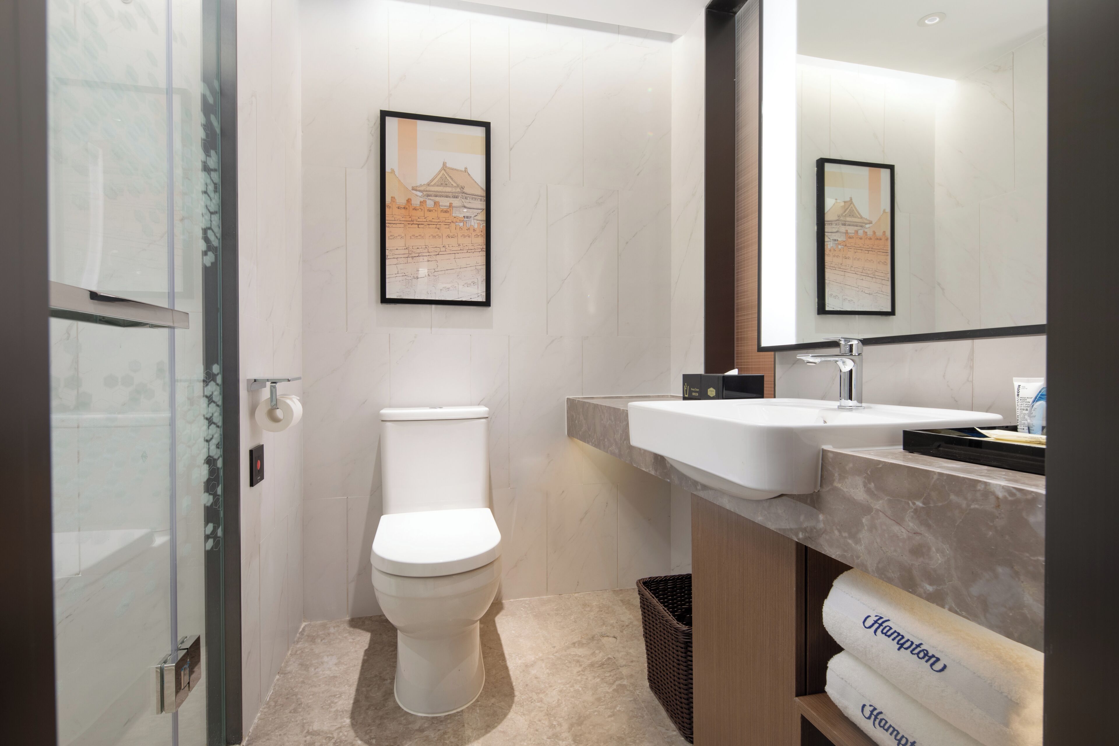 Un baño moderno con inodoro, lavamanos, cabina de ducha de vidrio y espejo.