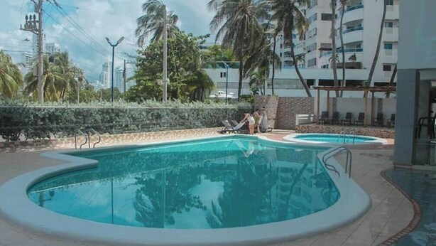 Una piscina de borde curvo, rodeada por un muro bajo y palmeras.